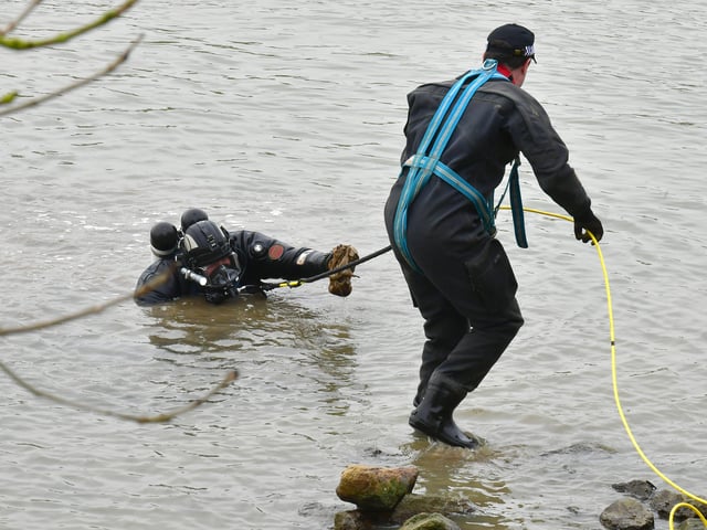 A police diver hands an object discovered in the river to a colleague. EMN-220203-142943001