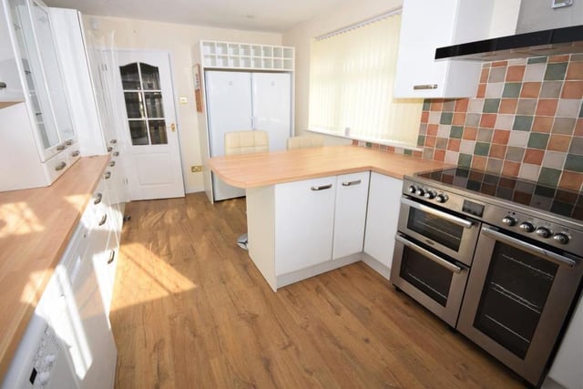 A second shot of the breakfast kitchen, which boasts modern appliances, including a Belling range cooker with extractor above, fridge, freezer, washing machine and dishwasher. The floor is laminated, and there are uPVC windows facing the front and side of the bungalow.