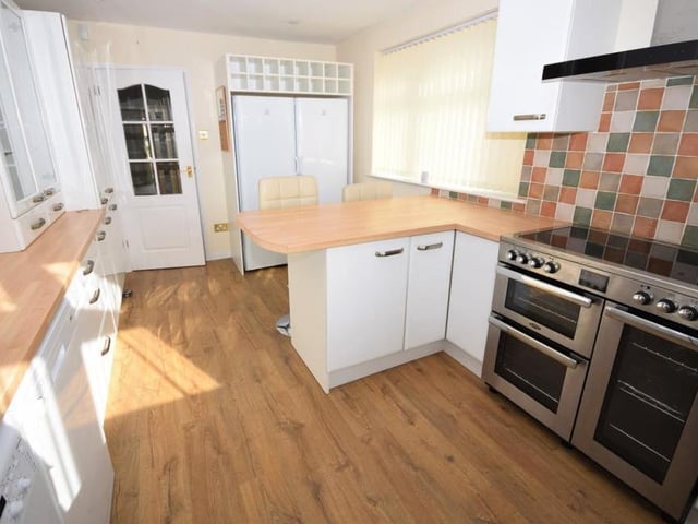 A second shot of the breakfast kitchen, which boasts modern appliances, including a Belling range cooker with extractor above, fridge, freezer, washing machine and dishwasher. The floor is laminated, and there are uPVC windows facing the front and side of the bungalow.